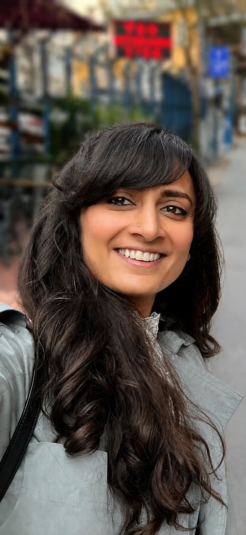 Sahana Vijai smiling on a city street, photographed outdoors in soft light.
